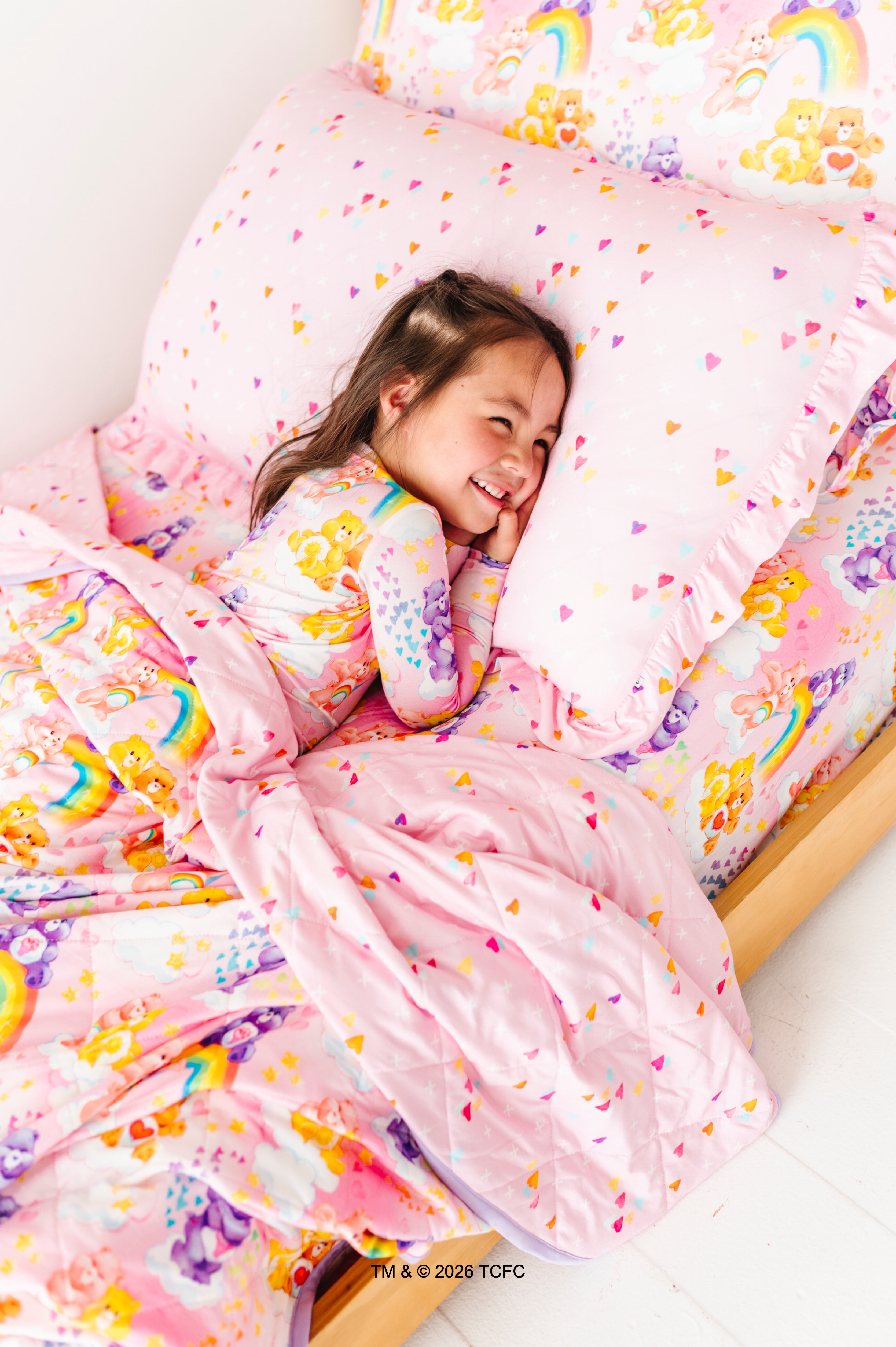 Child in a bed with colorful Care Bears™ bedding featuring rainbows and hearts
